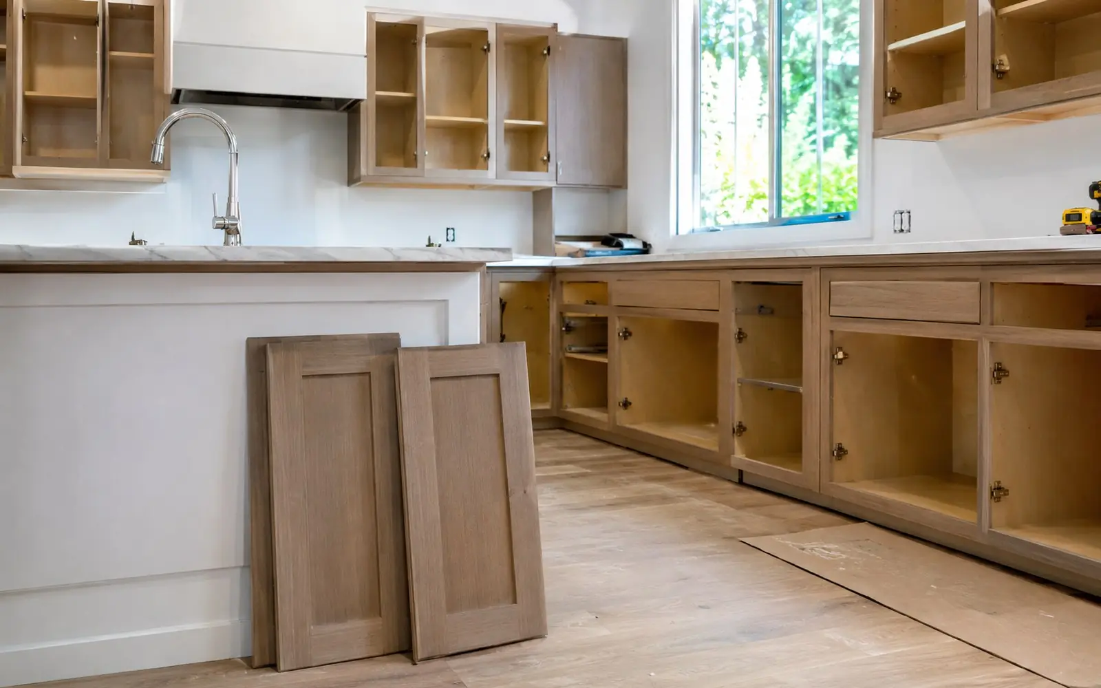 A kitchen mid-refacing, with the old cabinet doors removed, new veneer applied to the face frames and two new shaker doors leaning against the island.
