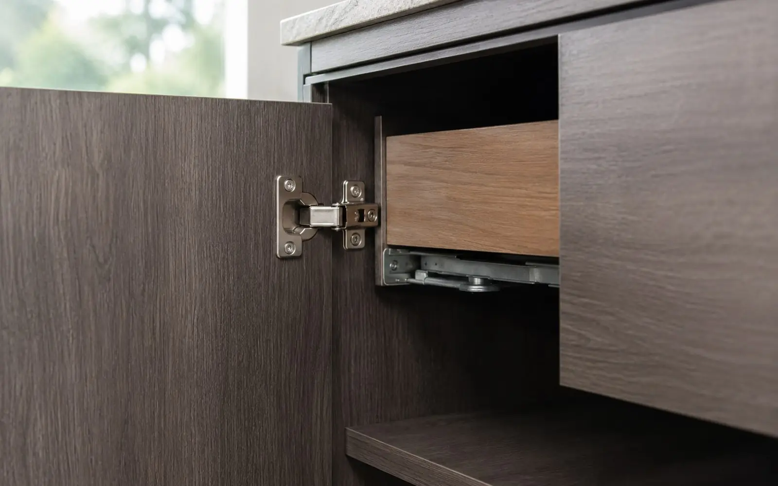 Close view of an open cabinet door showing a concealed cup hinge with adjustment screws, beside a drawer on undermount soft close slides.