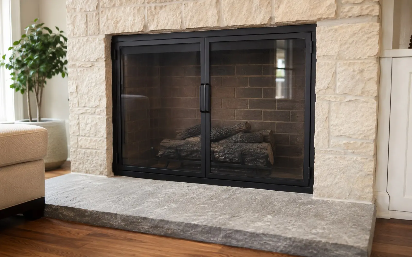 A pair of black steel and glass fireplace doors closed across a brick firebox, with a stone hearth extension running out across the floor in front of them.