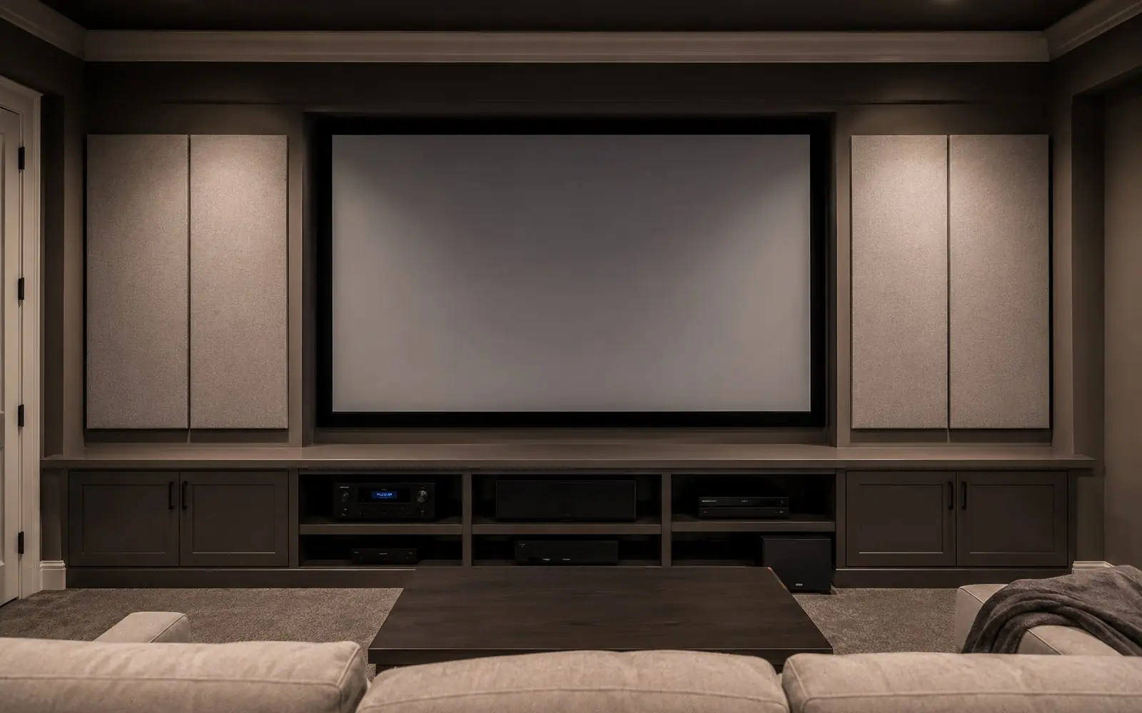 A media room wall with fabric wrapped acoustic panels either side of a screen and a low built-in cabinet holding AV equipment.