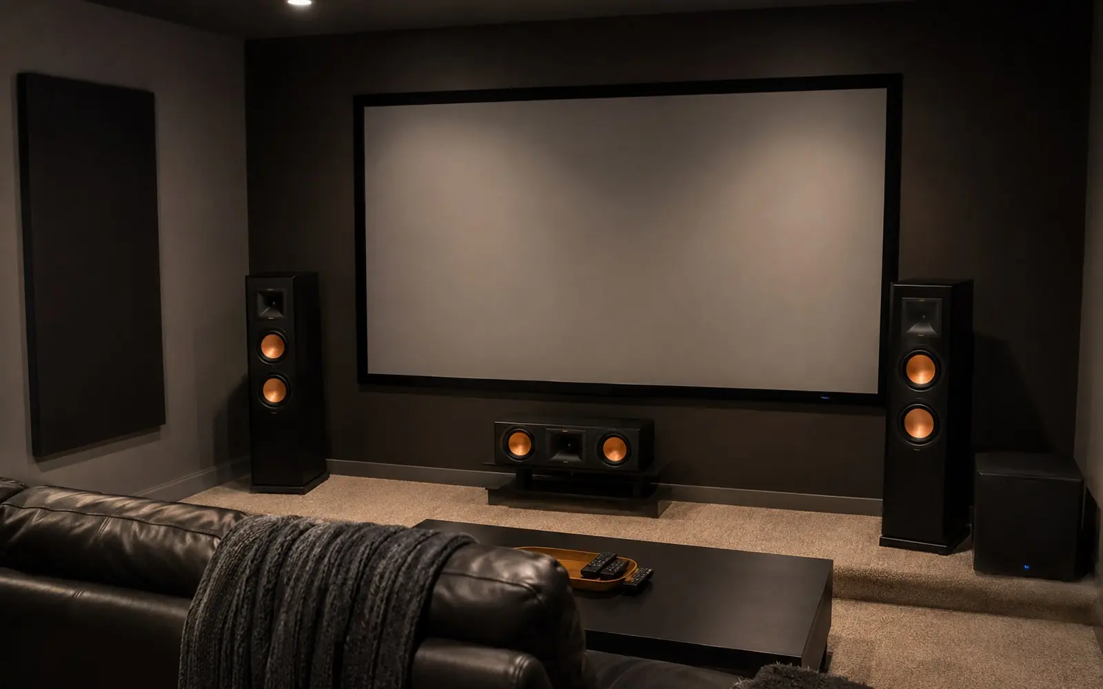 A dark media room with a floorstanding speaker either side of a large screen, a center speaker below it, and a subwoofer in the corner.