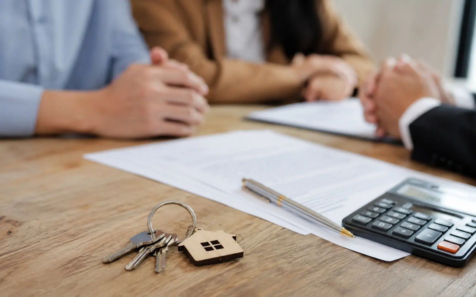 A closing table with a printed Closing Disclosure, a calculator and a pen, with a set of house keys beside the paperwork.