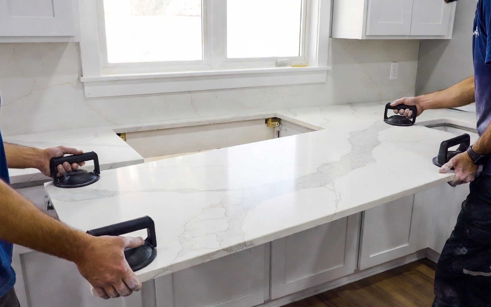 Two installers setting a quartz slab onto base cabinets, veining in daylight