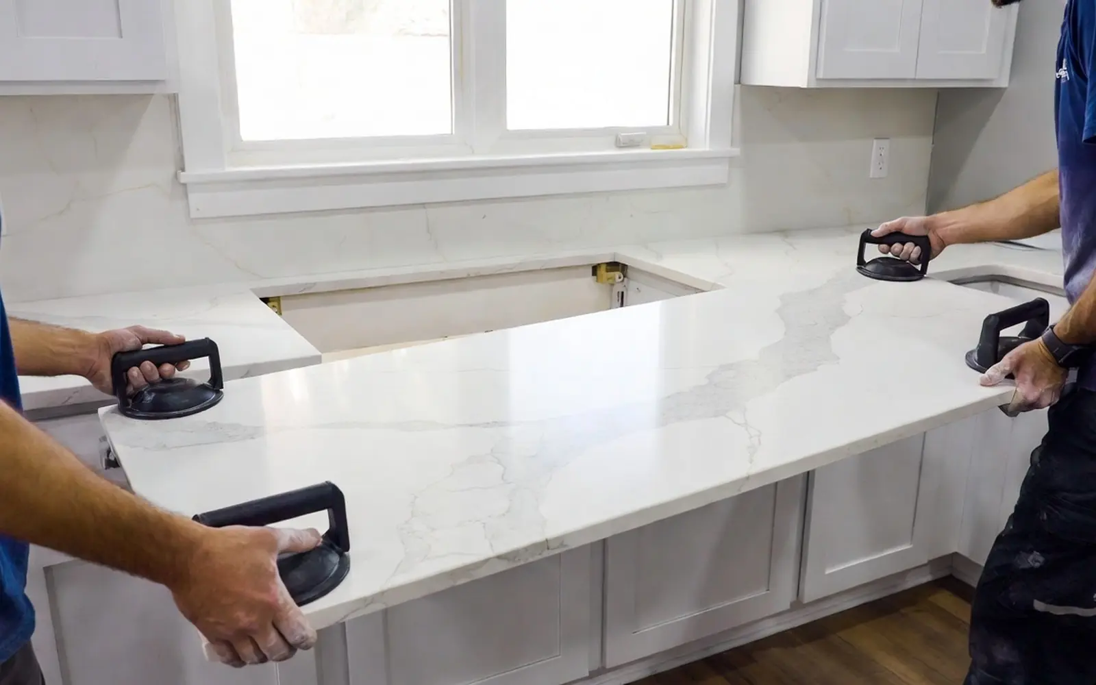 Two installers setting a quartz slab onto base cabinets, veining in daylight