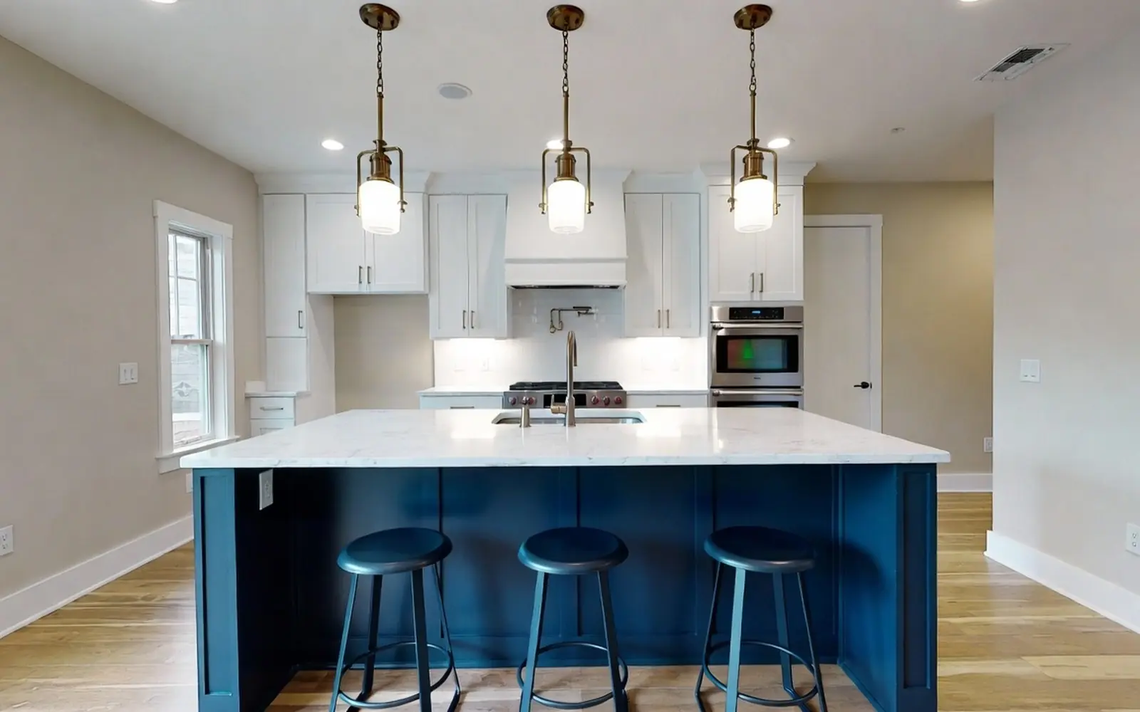Large navy-painted island with quartz top and seating for three, pendant trio above
