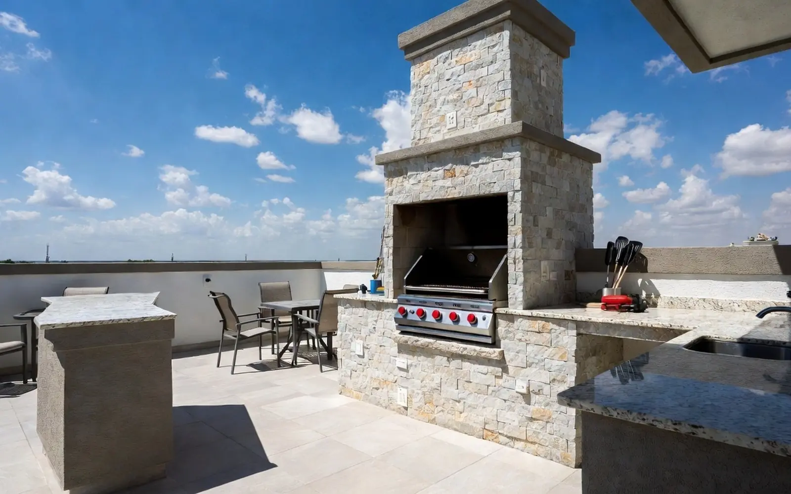 Built-in grill island with stone veneer on a sunny patio, prep counter, blue sky