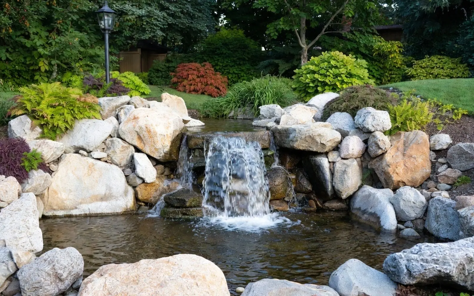 Small natural boulder waterfall and pond in a planted backyard corner