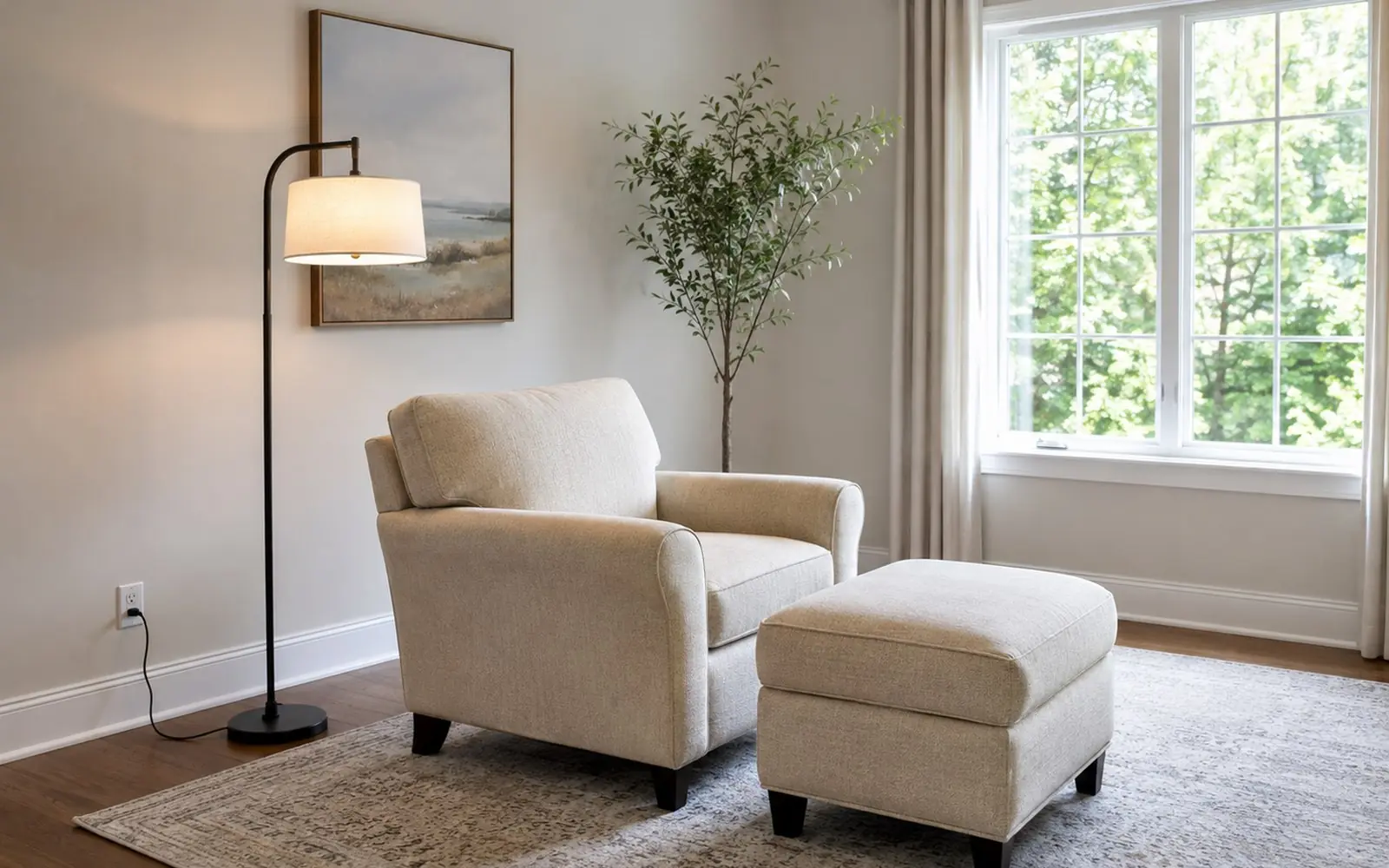 A single upholstered armchair with a matching ottoman placed near a window, angled away from the wall, with a floor lamp behind it and a power cord running to a wall outlet.