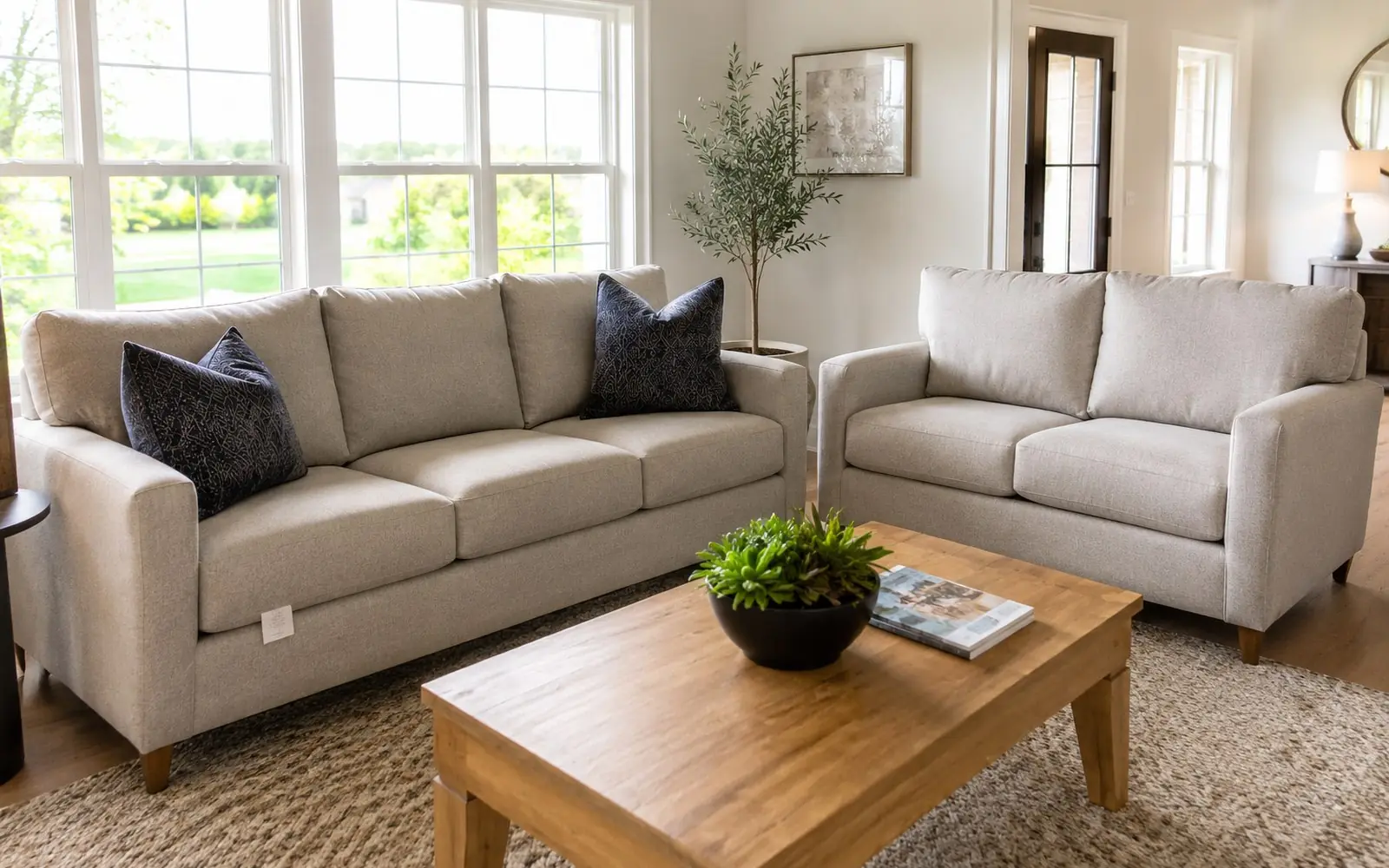 A three seat fabric sofa with loose back cushions beside a matching two seat love seat, both on wooden legs, with a permanent white tag visible under one seat cushion.