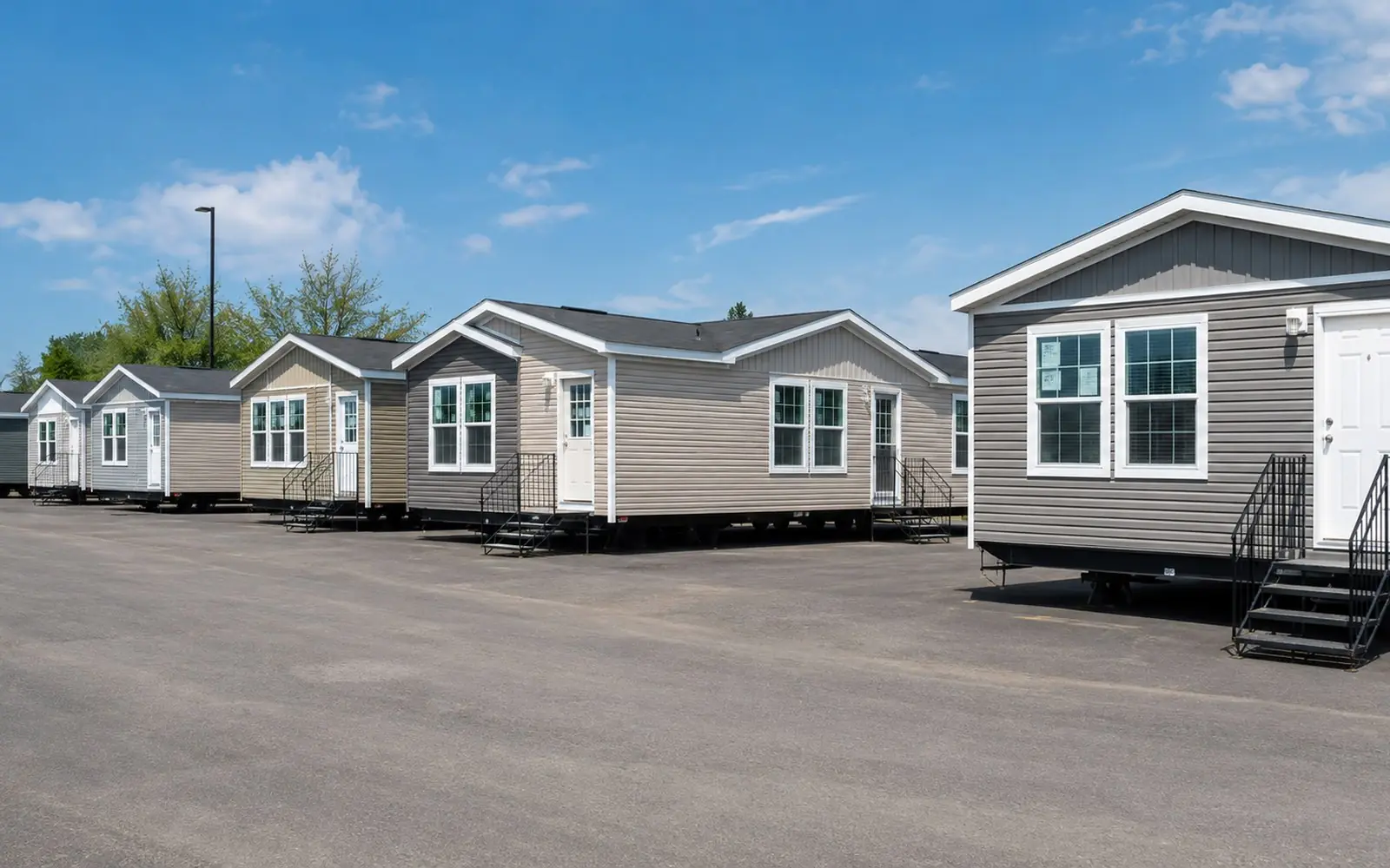 A row of new single-section and double-section manufactured homes lined up on a retailer's sales lot with window stickers still attached.