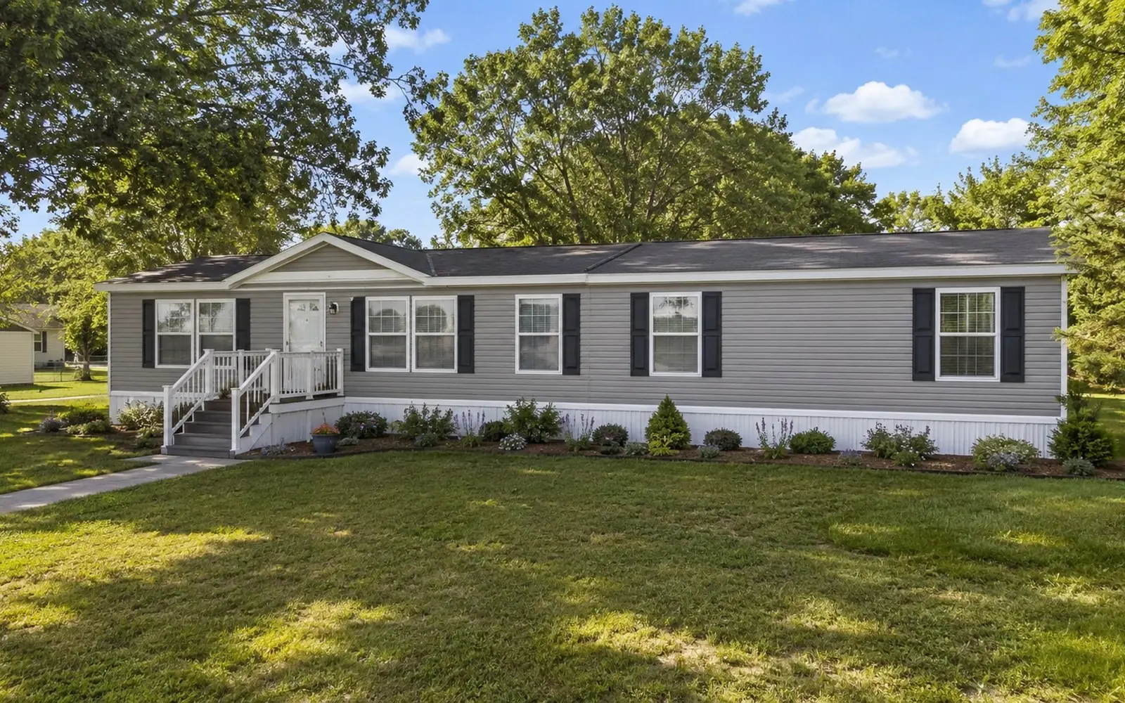 A double-section manufactured home on a residential lot with the two halves joined, siding installed, and the marriage line still visible along the roof ridge.
