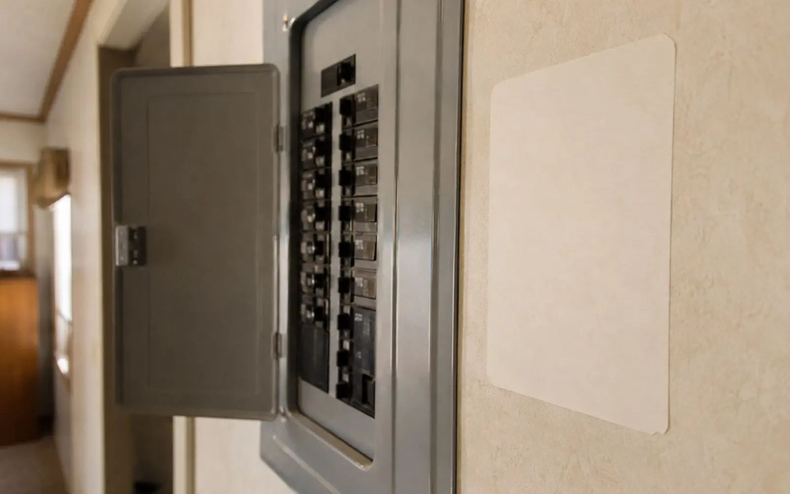 A blank data plate on the wall beside an open electrical panel inside a manufactured home.