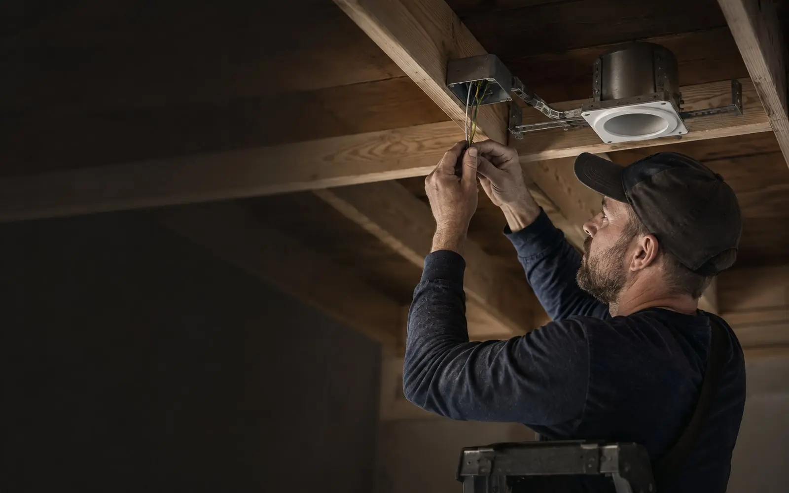 Electrician terminating wires in an open ceiling junction box beside a recessed light housing